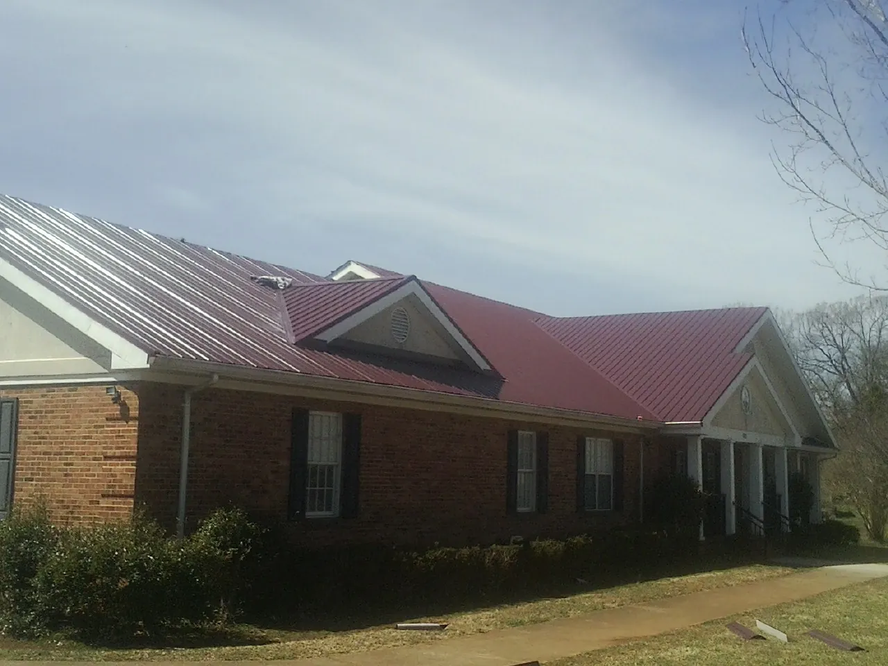 Red metal roof with gabled entries on a long brick building, from a Hail Damage Roof Repair job in Garden City