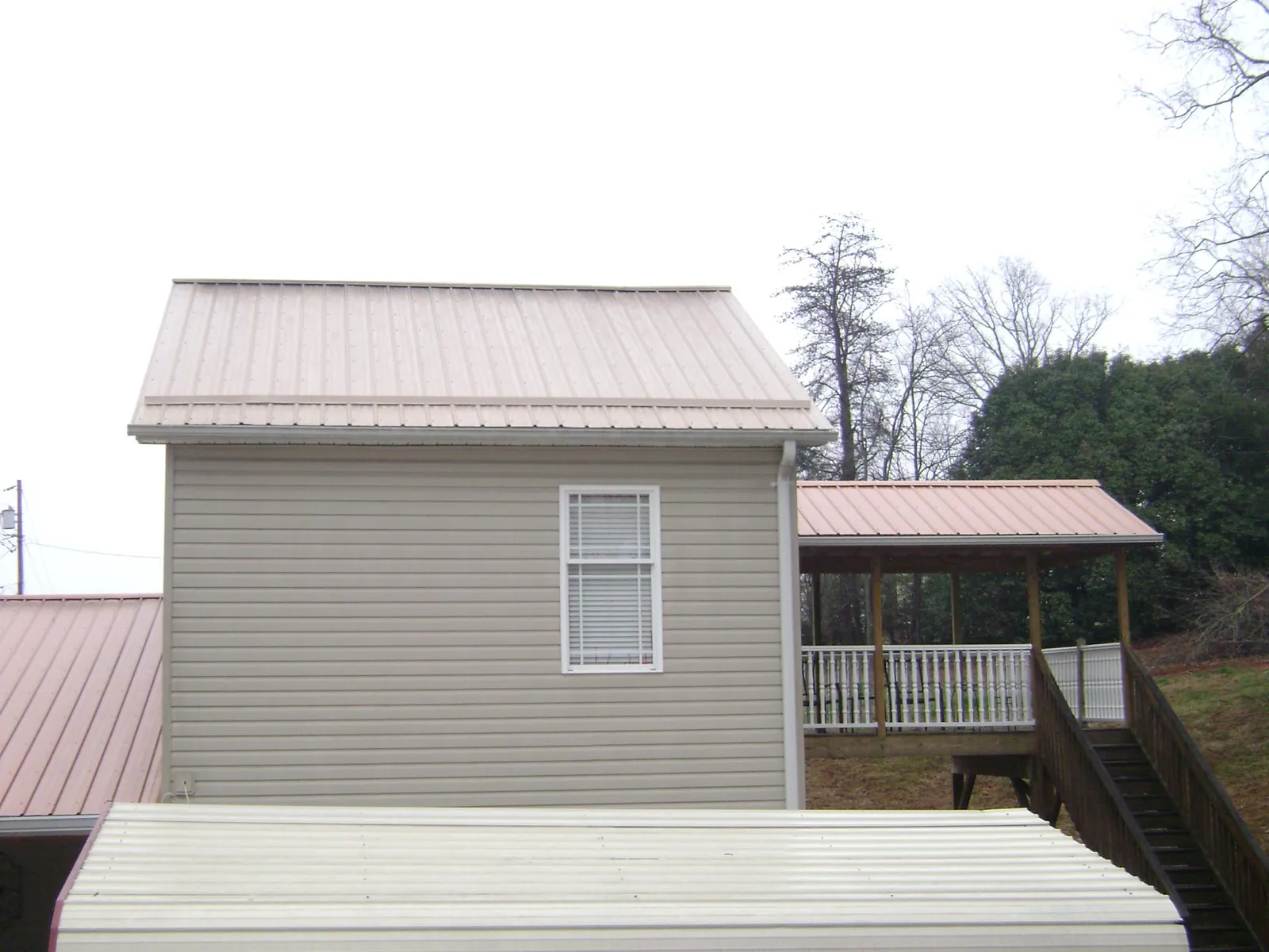 Tan metal roofs on a two story addition and attached porch, from a Roof Replacement job in Garden City